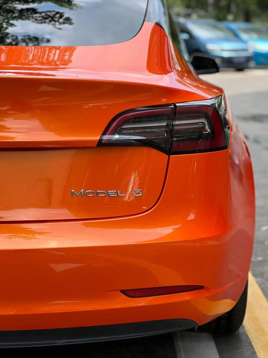 Detailed view of Neon Gold Orange vinyl on Tesla Model 3 rear-right - seamless panel coverage - Kaleido