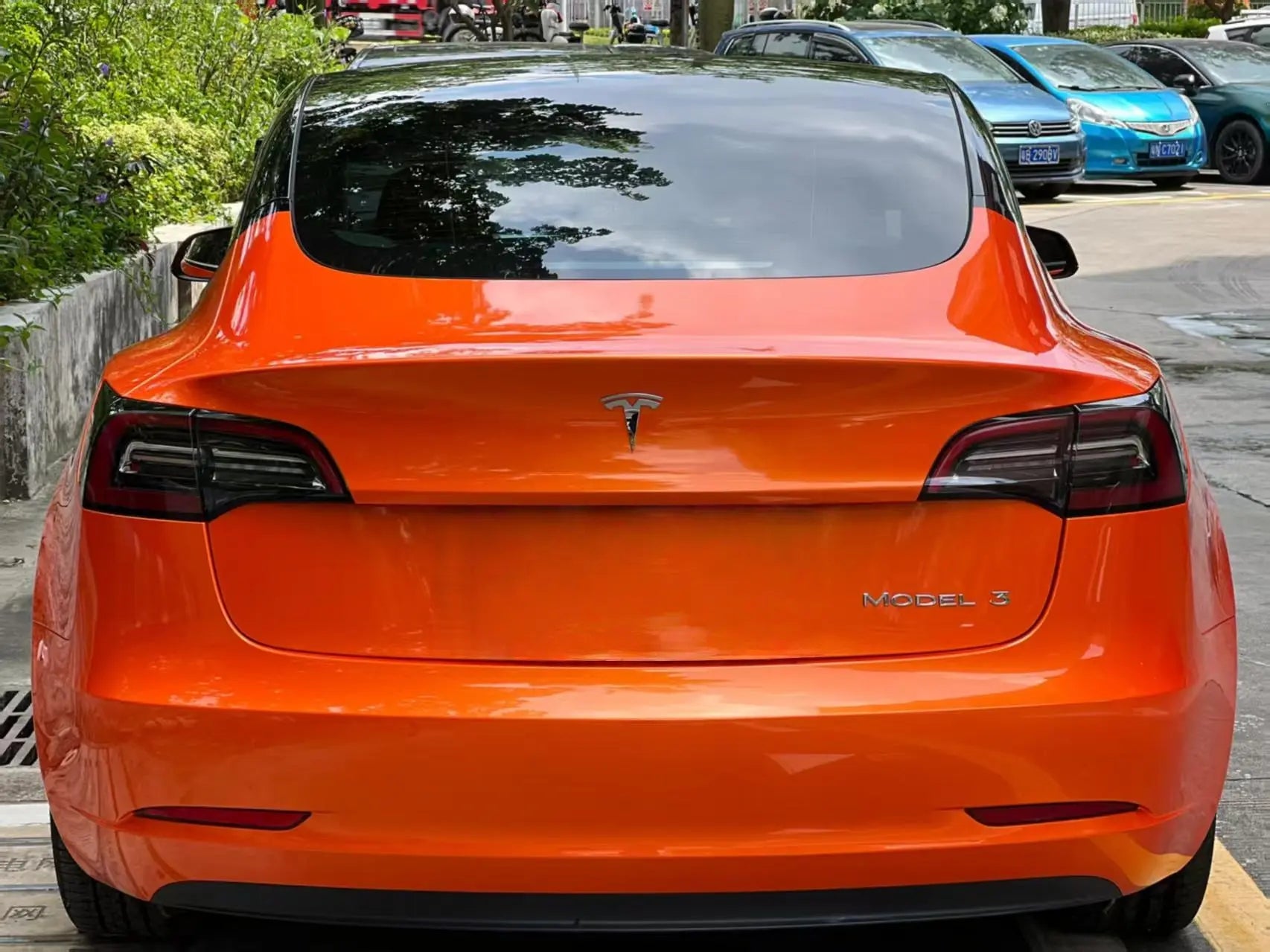 Tesla Model 3 in Neon Gold Orange color shift wrap - rear view showing gold to orange transition on sedan design - Kaleido