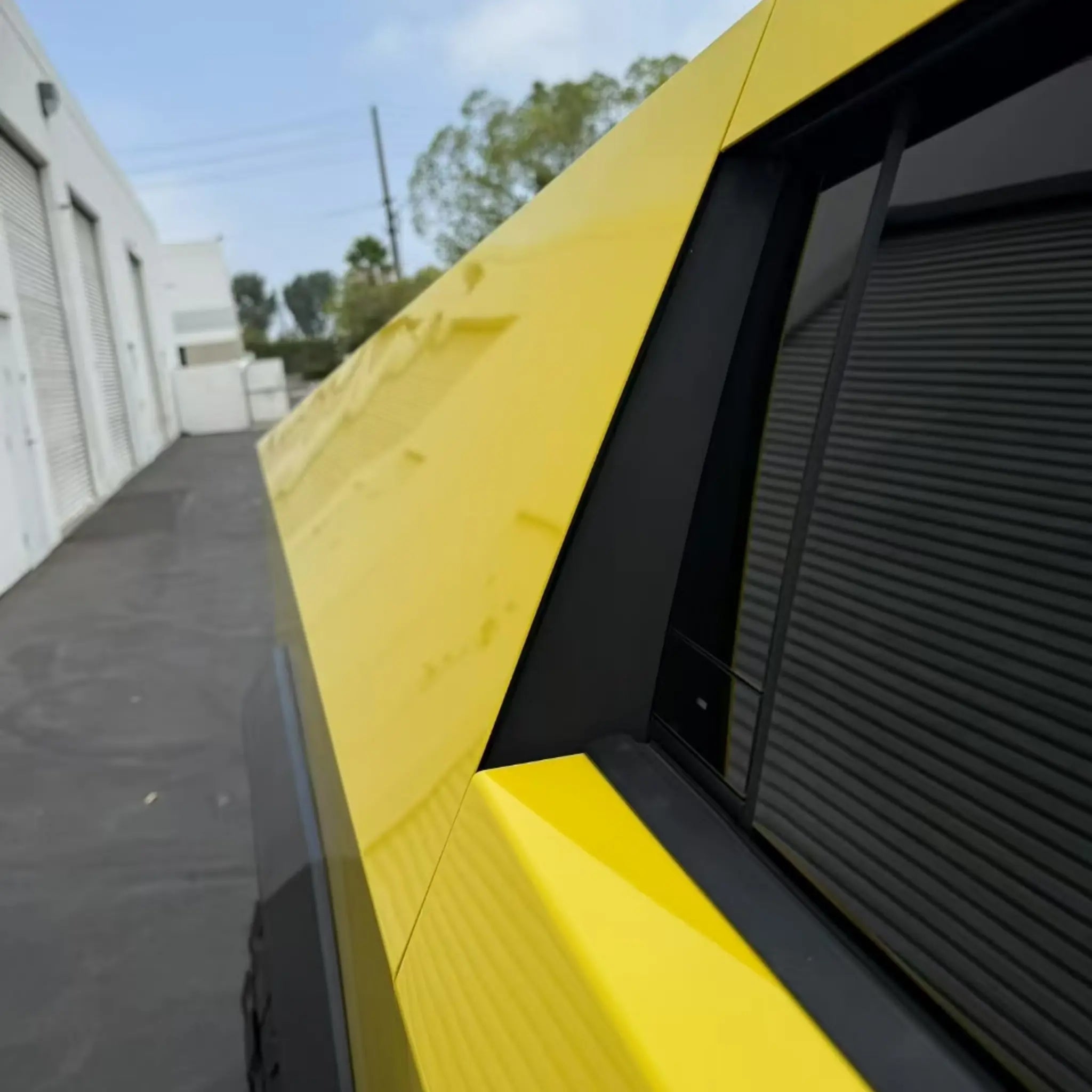 Close-up detail of Gloss Corn Yellow wrap on the Tesla Cybertruck's rear fender and body seam - Kaleido