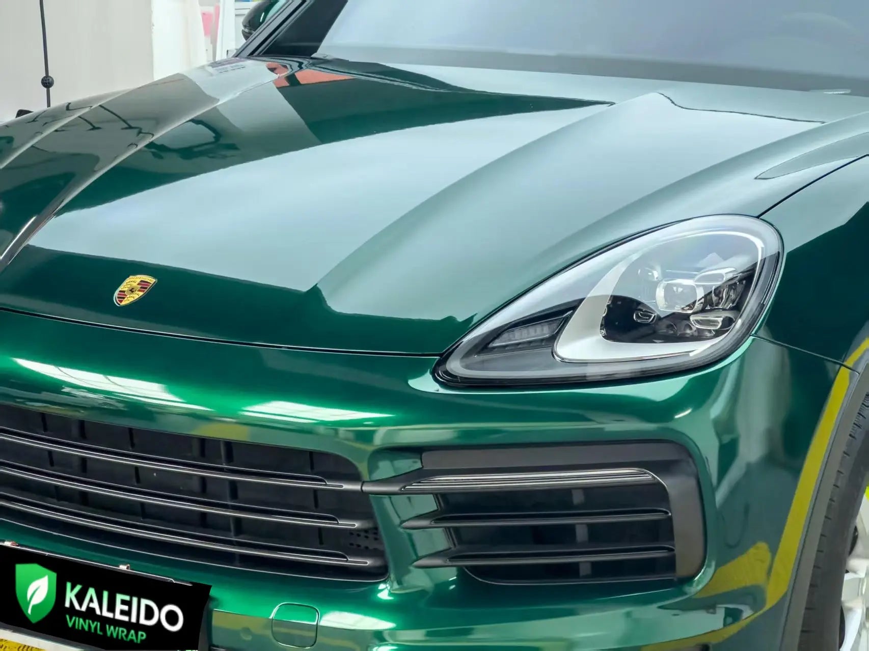 Detailed shot of Gloss Metallic Agate Green vinyl on Porsche Cayenne front-left area - Kaleido