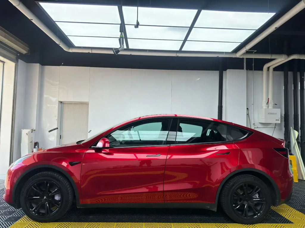 Tesla Model Y with Gem Red metallic wrap - indoor side view showing glossy finish - Kaleido