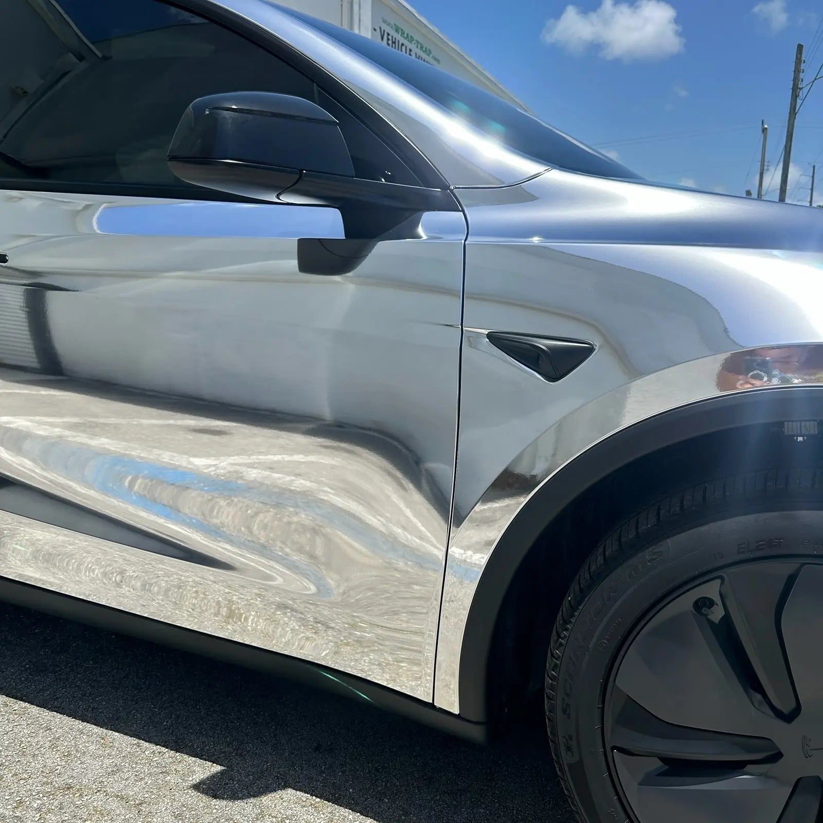 Detailed shot of Mirror Chrome Silver wrap on Tesla Model Y front-right bumper - precise mirror surface - Kaleido