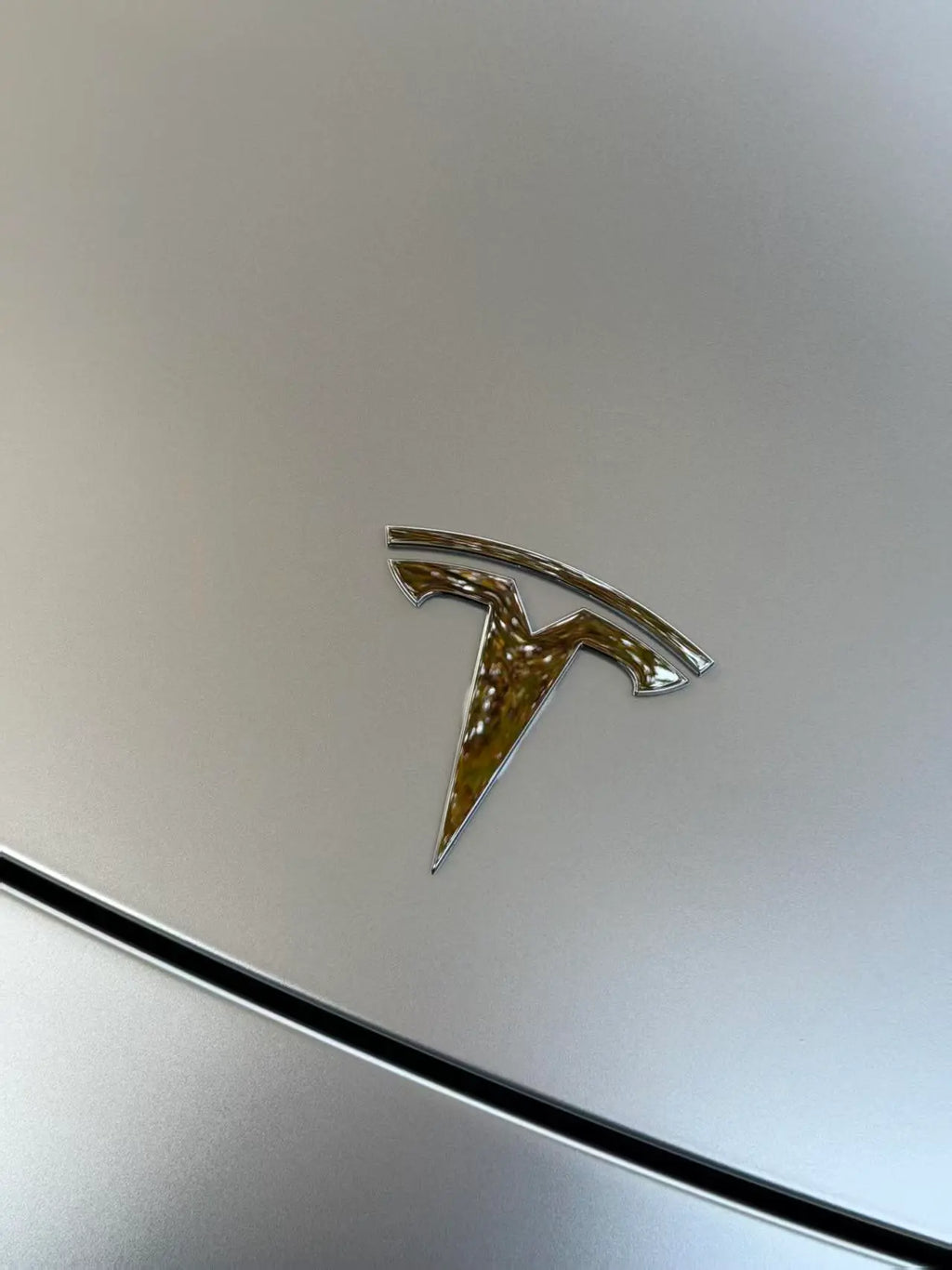 Extreme close-up of the Tesla emblem area on the hood of a Model Y wrapped in Satin Chrome Alexander Silver - Kaleido