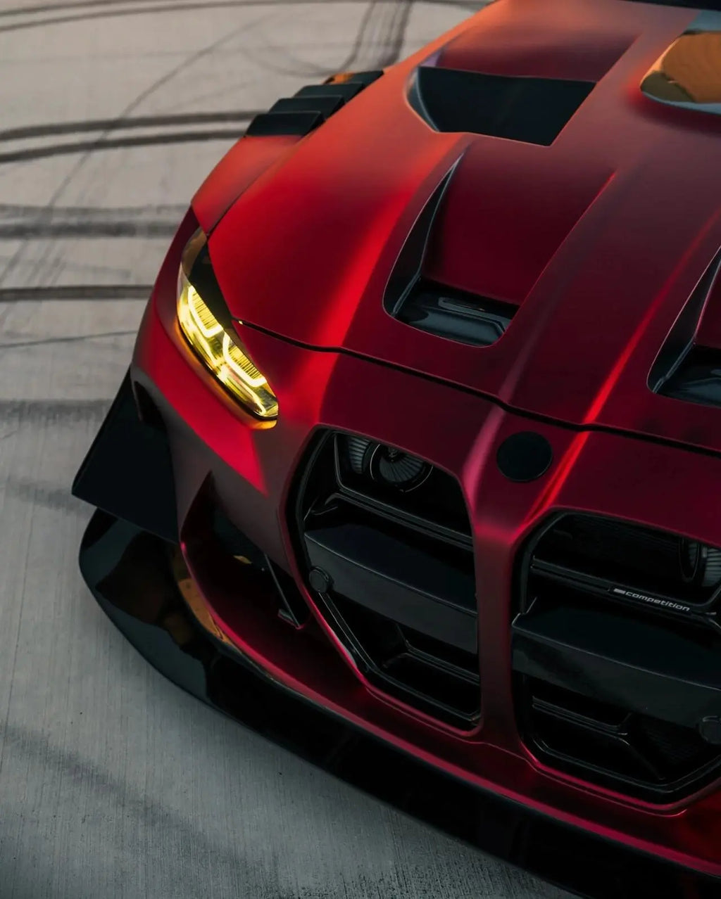 Macro detail of Satin Chrome Romanee Red vinyl on BMW M4 right front corner - Kaleido