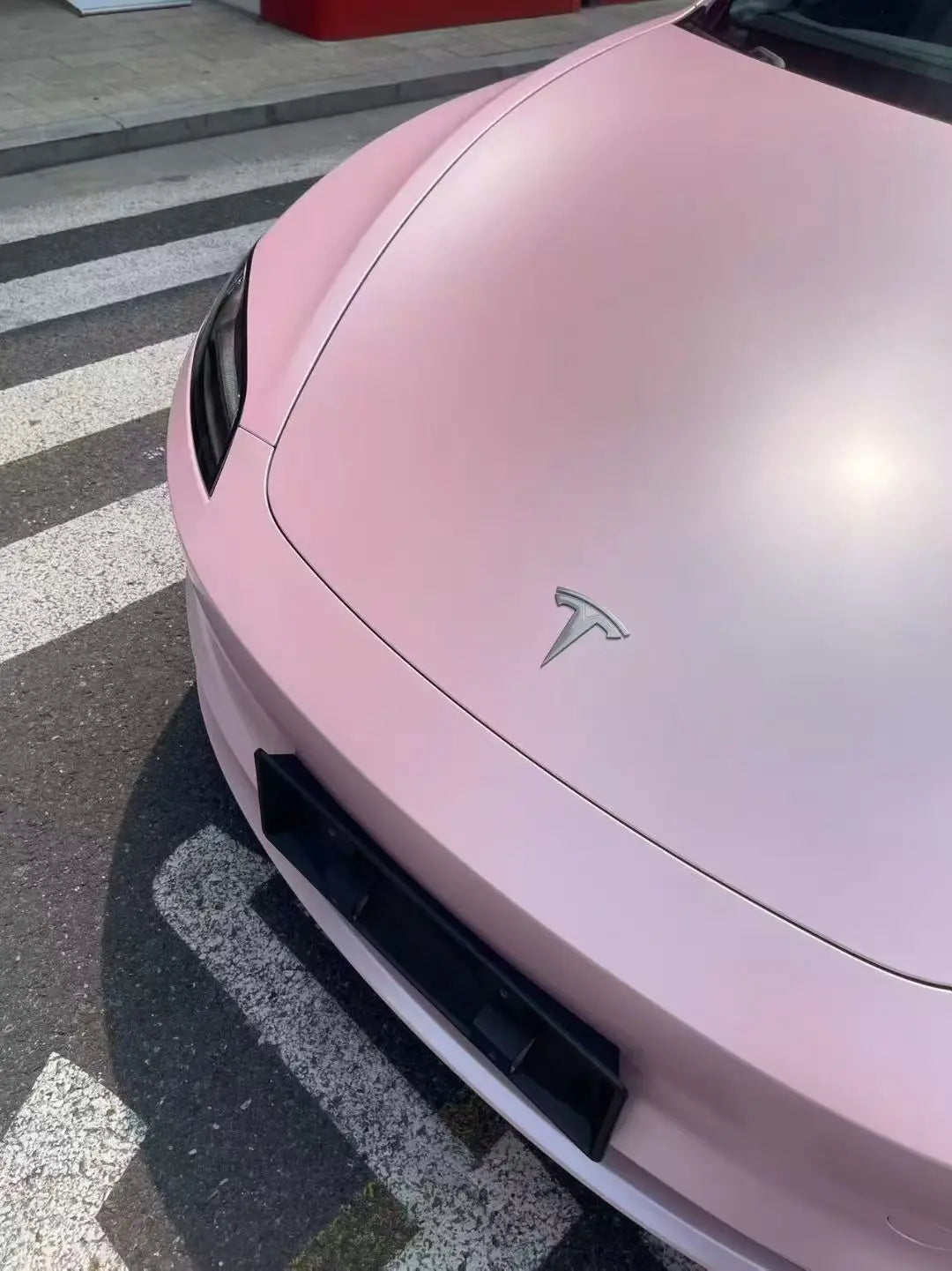 Close-up detail of Satin Metallic Sakura Pink vinyl on a Tesla Model 3 hood, showcasing the metallic sheen - Kaleido